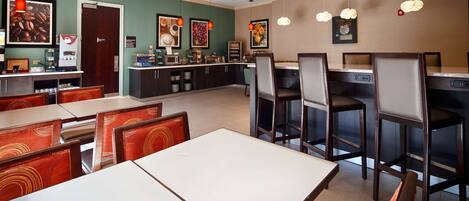 A restaurant with booths and high tables, a coffee machine, and various food displays.