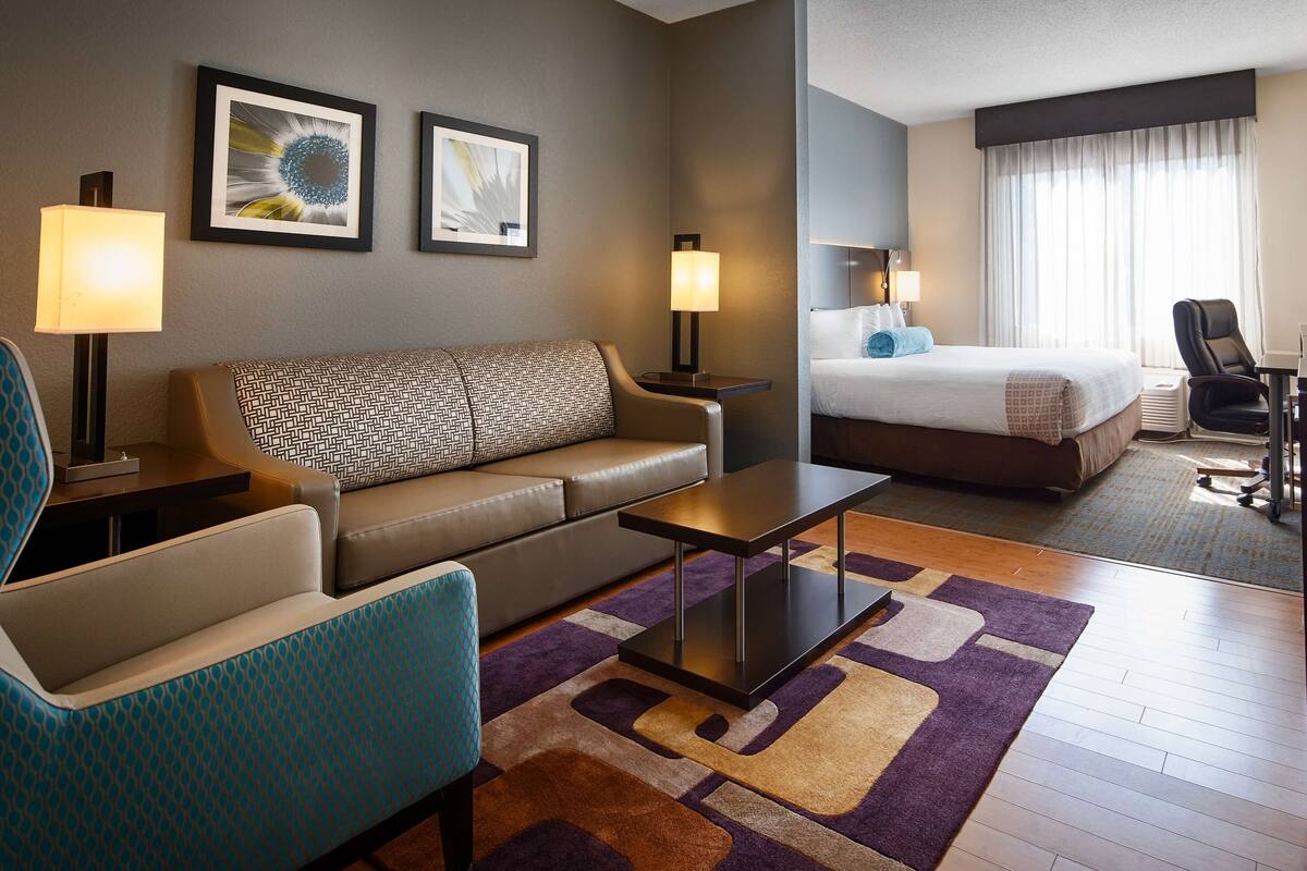 A hotel room with a sofa, a bed, a desk, and two framed pictures on the wall.