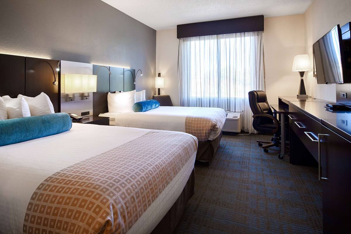 A hotel room with two beds, a desk, a chair, a TV, and a window with curtains.