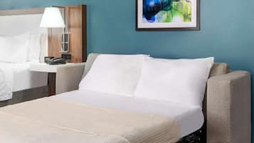 Une chambre d’hôtel avec un lit, une table de chevet avec une lampe, un téléphone et un tableau abstrait encadré accroché au mur.