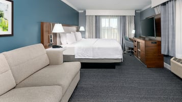 Ein Hotelzimmer mit Bett, Sofa, Schreibtisch, Fernseher und einem großen Fenster mit Vorhängen.