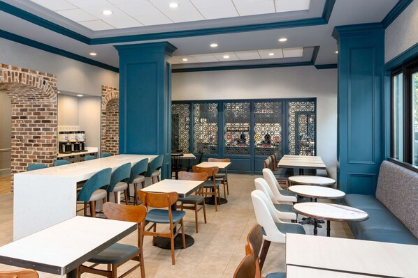 Interior moderno de restaurante con pared de ladrillo, detalles azules y diferentes opciones de asientos, incluyendo mesas y un banco.