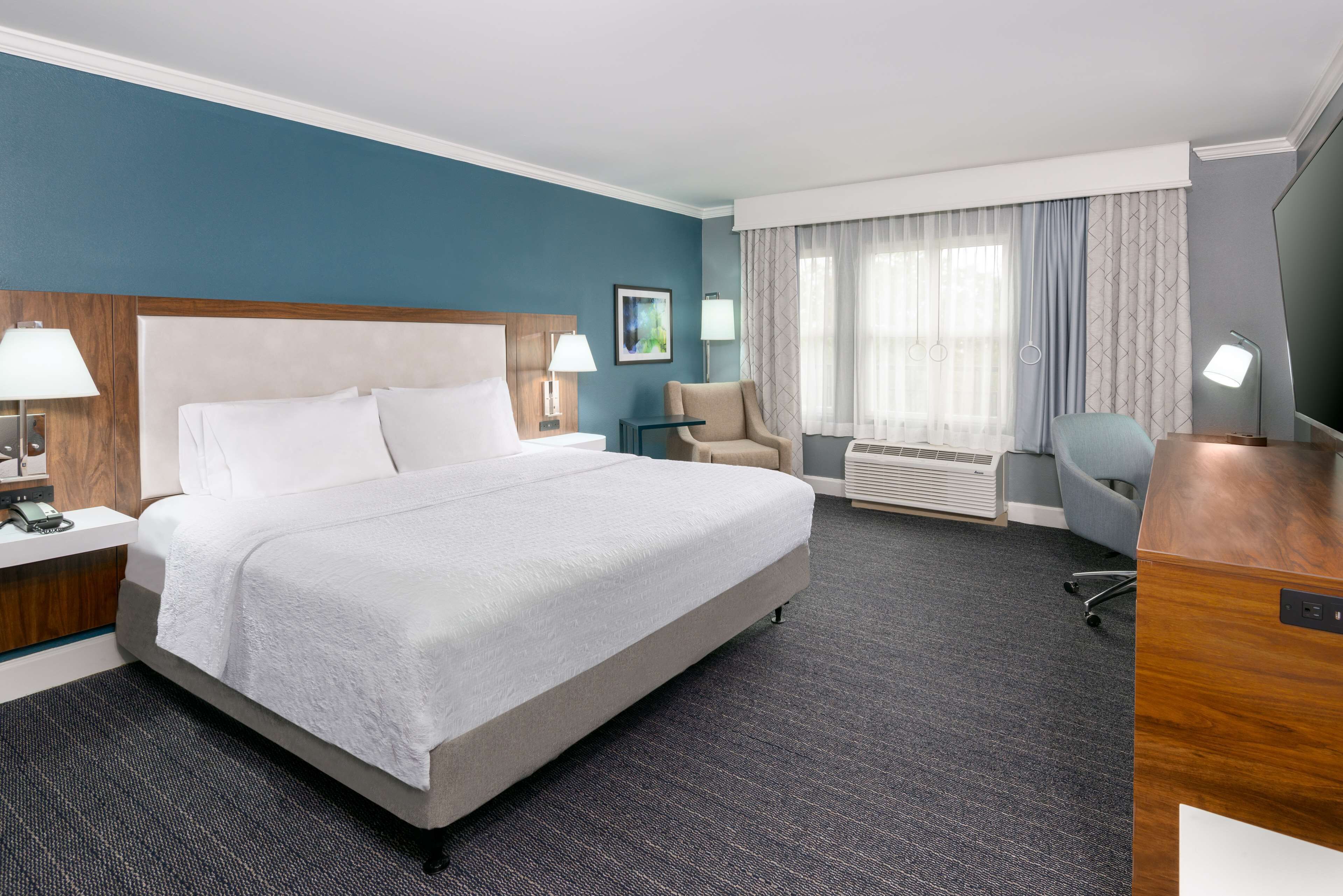 A hotel room with a large bed, a desk, a chair, a lamp, and a picture on the wall.