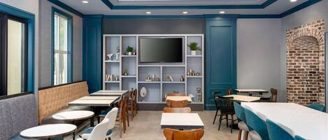 Un comedor con mesas y sillas, un televisor de pantalla plana grande y estantes con objetos decorativos.