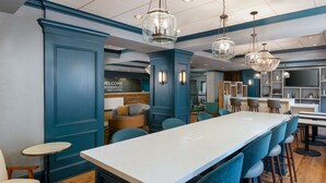 A modern bar area with a long counter, blue chairs, and hanging light fixtures. - Hampton Inn Savannah-Historic District (Savannah)