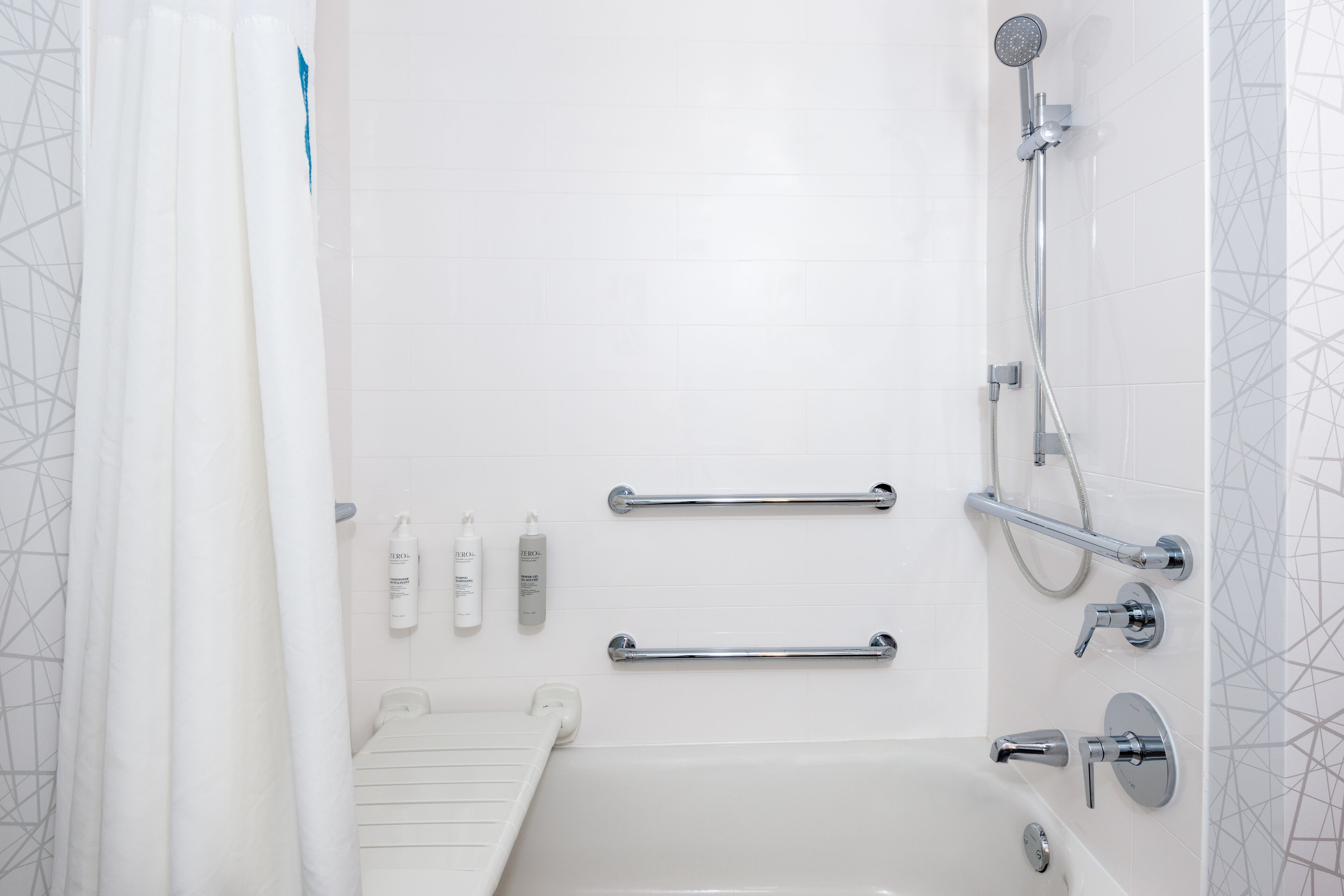 A modern bathroom with a bathtub, shower, and handrails.