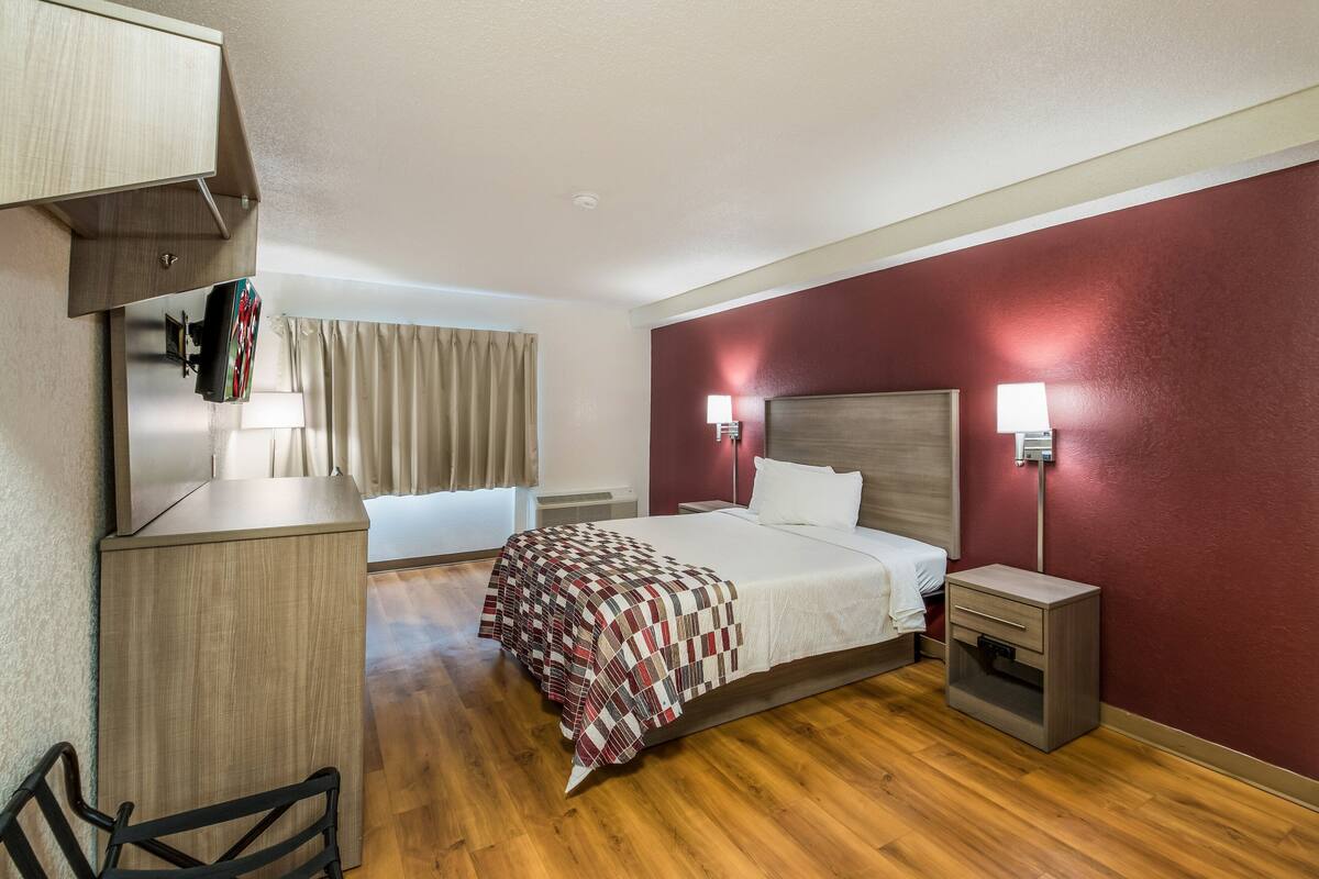 A hotel room with a bed, bedside table, lamp, and a desk with a chair.
