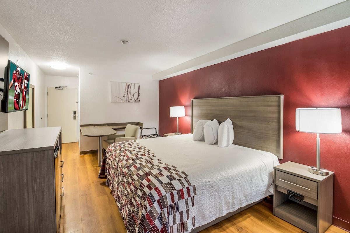 Habitación de hotel con una cama grande, dos mesitas de noche con lámparas, un escritorio, una silla y un televisor en la pared.