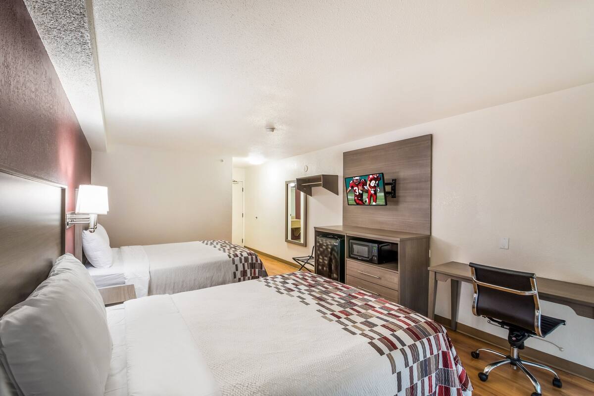 A hotel room with two beds, a desk, a chair, a TV, and a microwave.