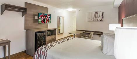 Una habitación de hotel con cama, escritorio, televisión, microondas y espejo.