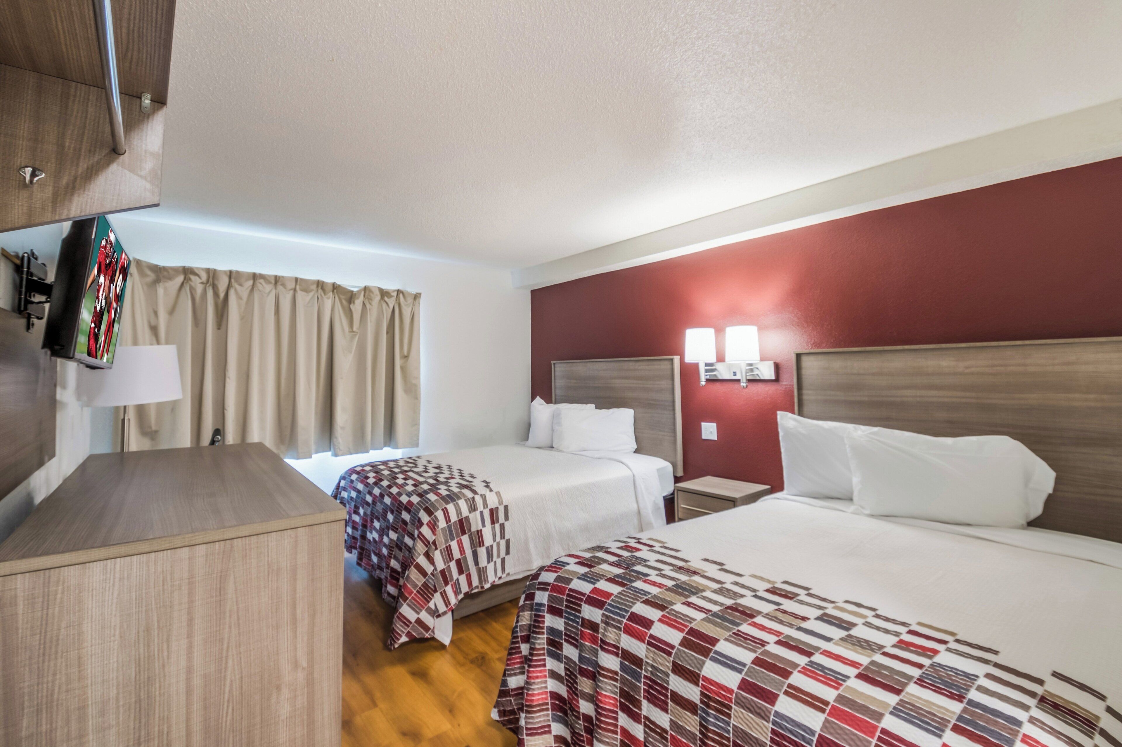 A hotel room with two beds, a desk, a lamp, and a TV mounted on the wall.