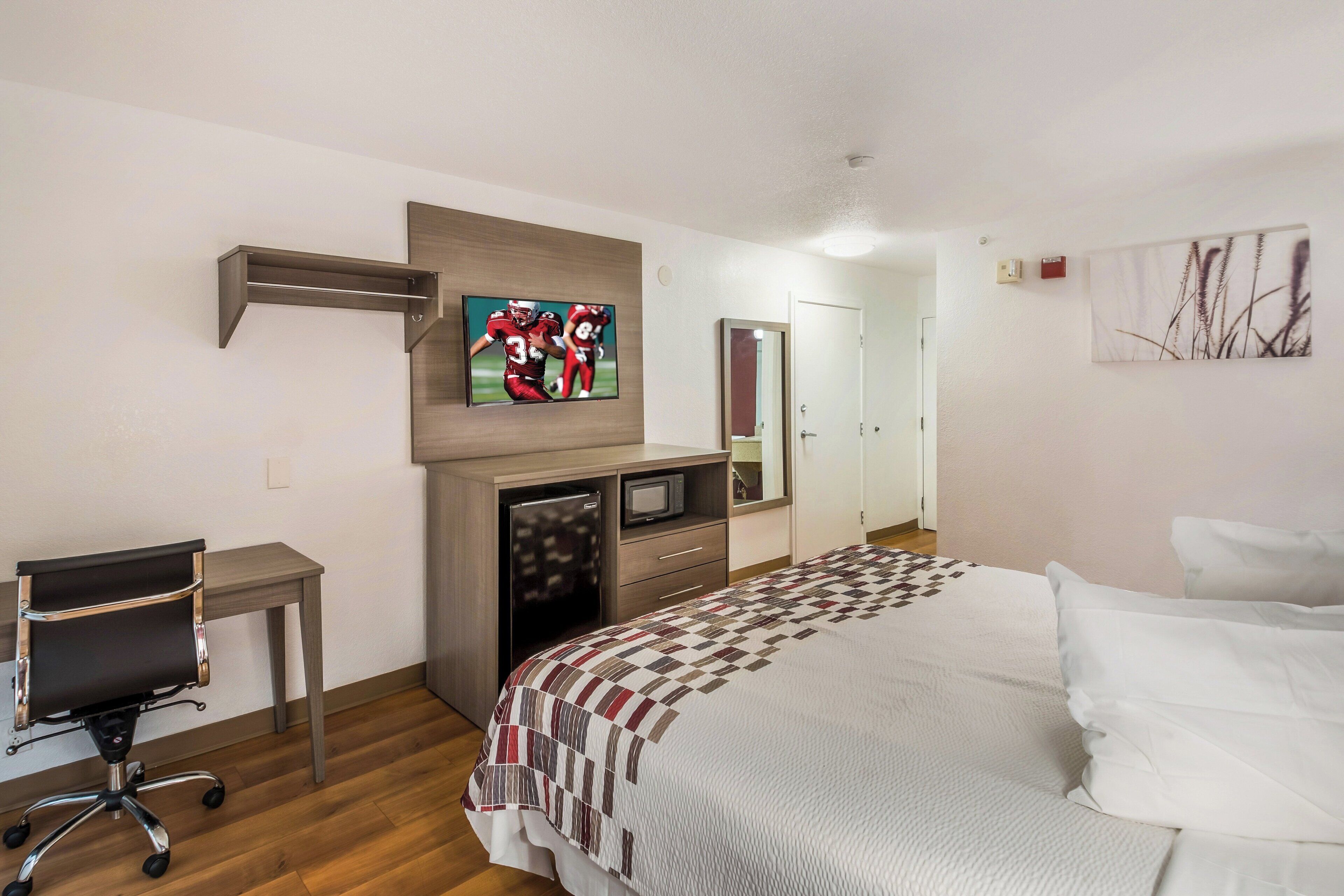 A hotel room with a bed, a desk, a television, a refrigerator, and a door.