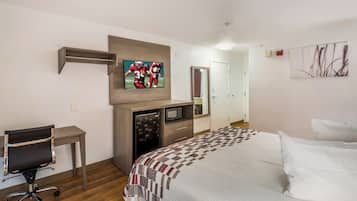 A hotel room with a bed, a desk, a television, a refrigerator, and a door.