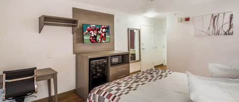 A hotel room with a bed, a desk, a television, a refrigerator, and a door.