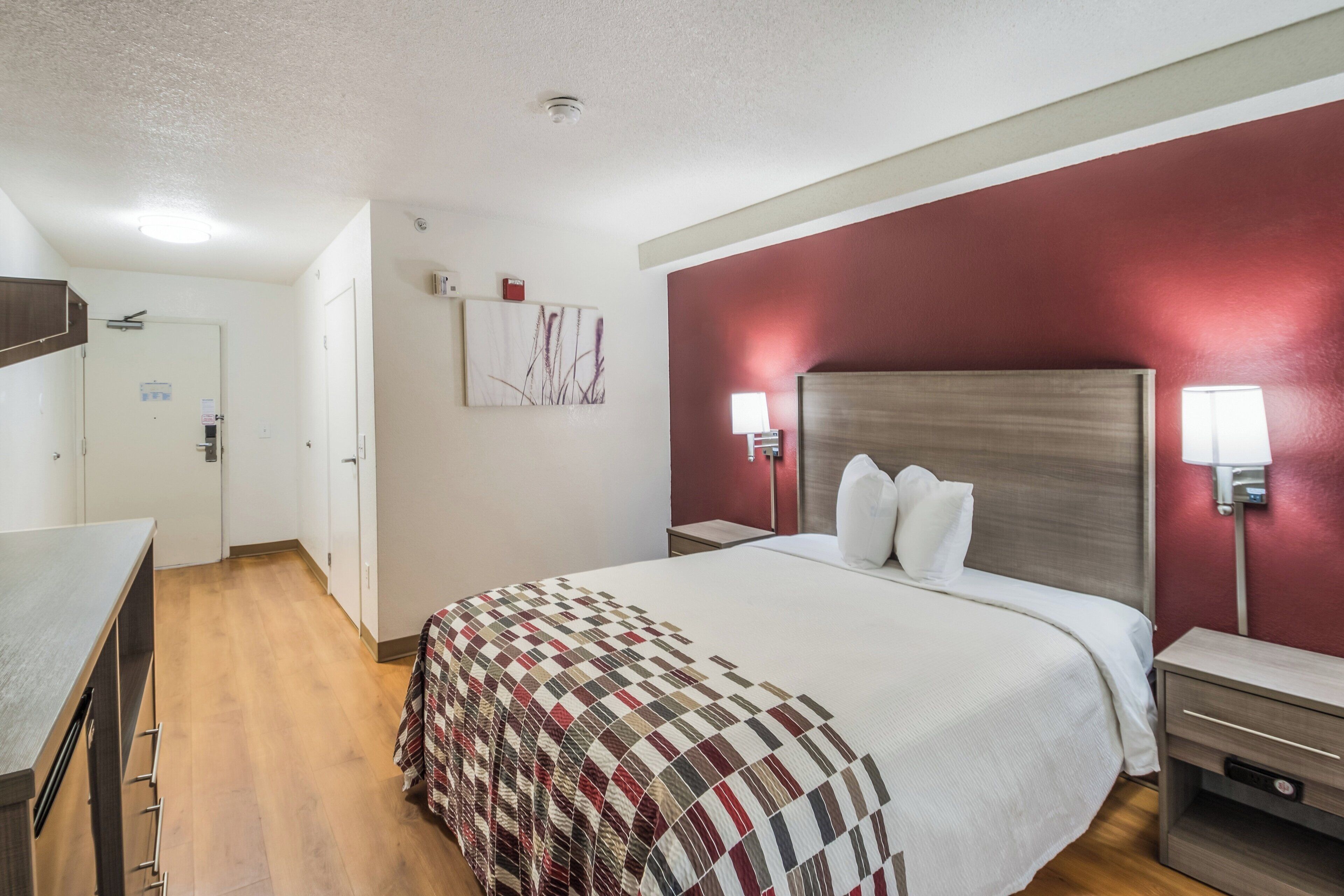 A hotel room with a bed, bedside tables, a desk, and a door.