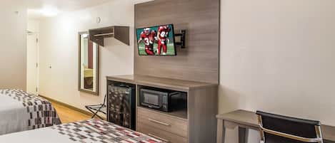 Une chambre d’hôtel avec deux lits, un bureau avec une chaise, un four à micro-ondes, un réfrigérateur et un téléviseur à écran plat fixé au mur.
