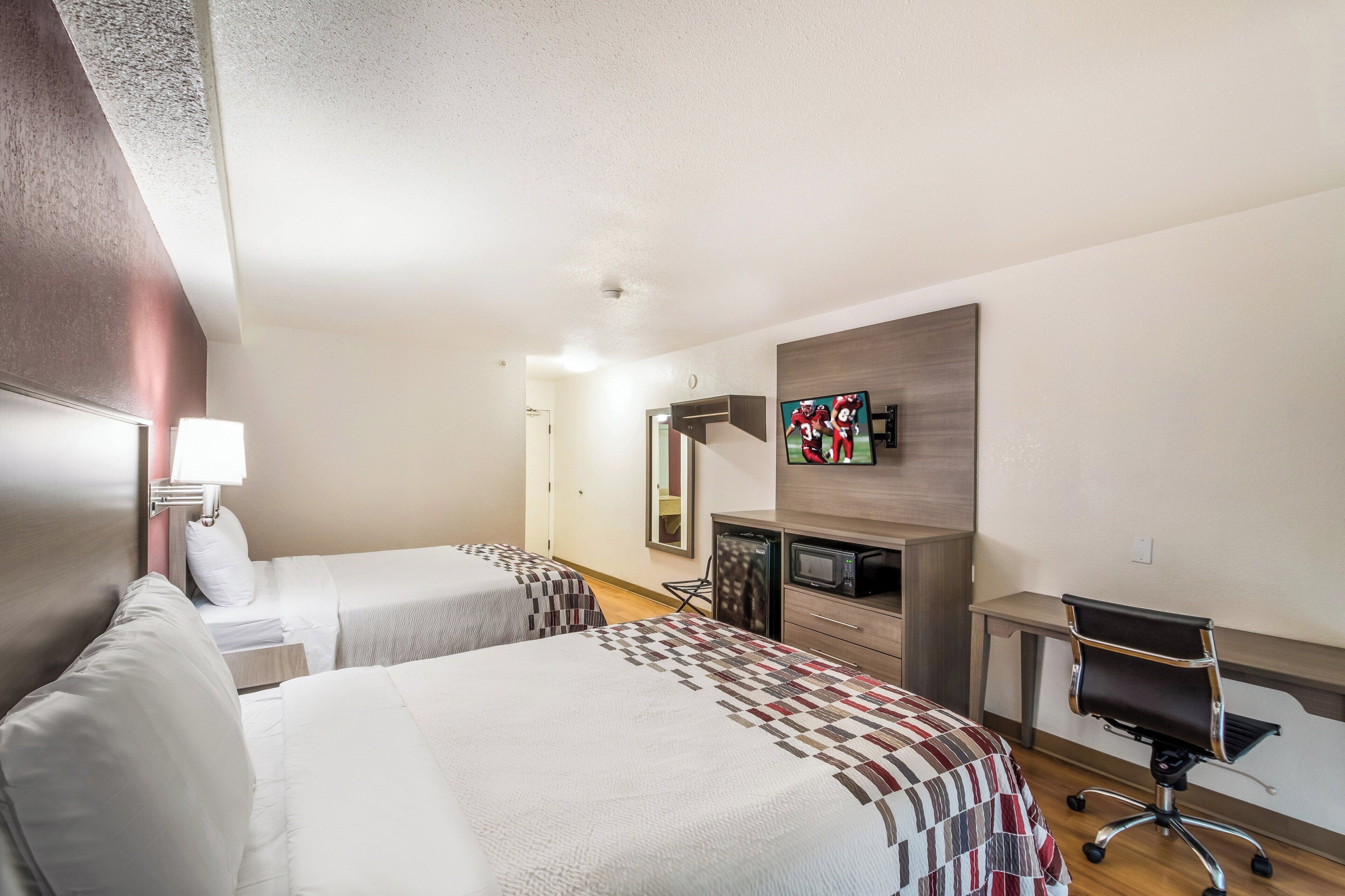 A hotel room with two beds, a desk with a chair, a television, and a microwave.