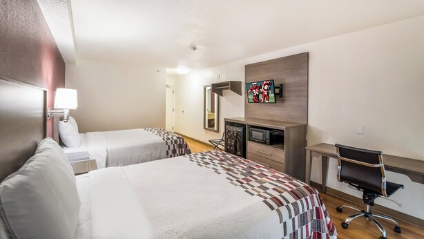 A hotel room with two beds, a desk with a chair, a television, and a microwave. - Red Roof Inn Rochester – Airport (Rochester)