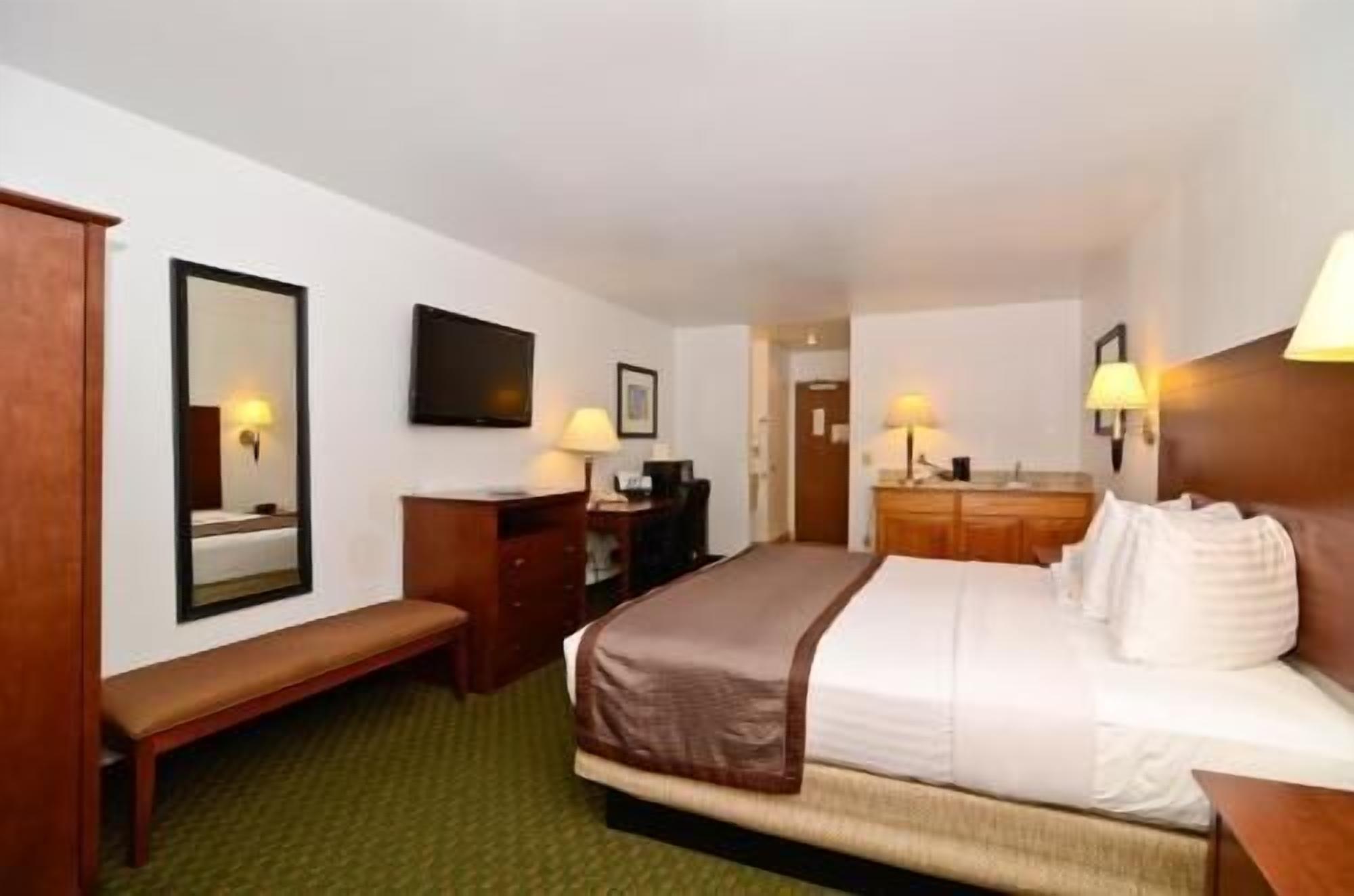 A hotel room with a bed, a desk, a chair, a mirror, a television, and a bathroom.