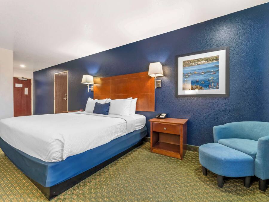 Habitación de hotel con una cama grande, dos lámparas de noche, una mesita de noche, una silla y un cuadro en la pared.