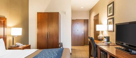 A hotel room with a bed, a desk with a television, a chair, a desk lamp, a telephone, and a wardrobe.