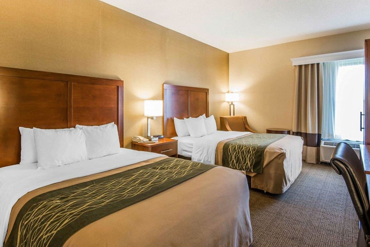 A hotel room with two beds, a desk, a chair, a lamp, and a window with curtains.