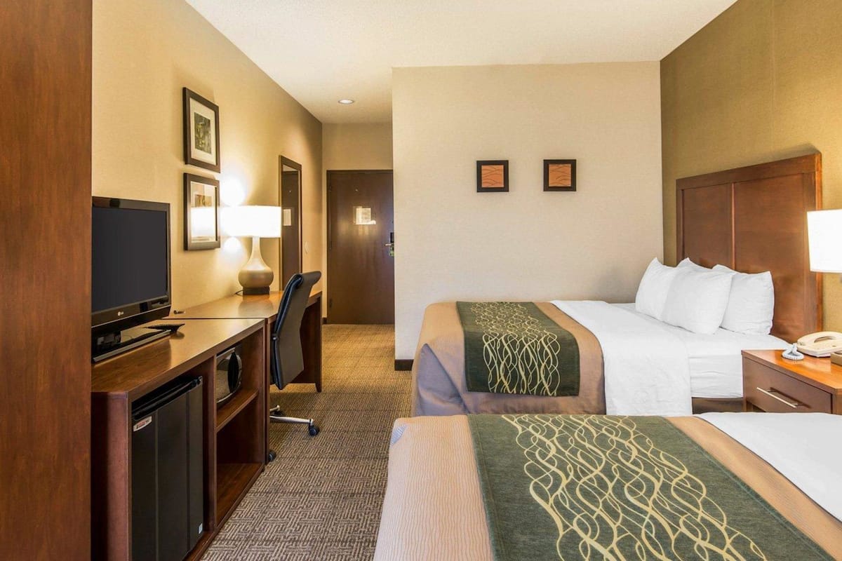 A hotel room with a bed, a desk with a TV, a chair, and a small kitchenette.