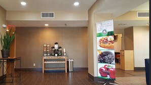 A reception area with a coffee station, a potted plant, and a banner promoting breakfast.