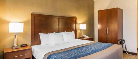 A hotel room with a large bed, two bedside lamps, a wooden wardrobe, a desk with a lamp, and a chair.