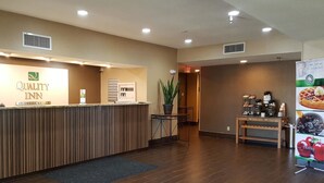 A reception area with a reception desk, a plant, a coffee station, and a sign for breakfast.