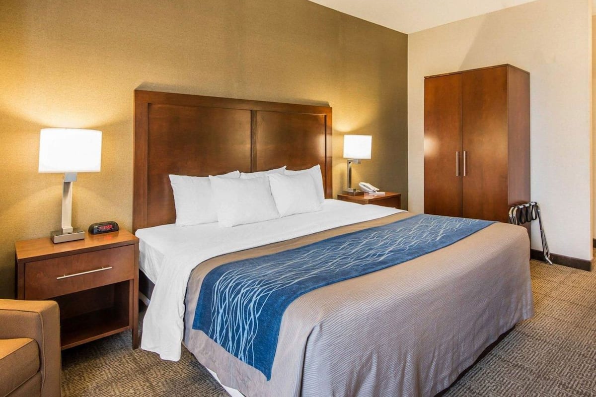 A hotel room with a bed, two bedside lamps, a nightstand, a wardrobe, and a chair.