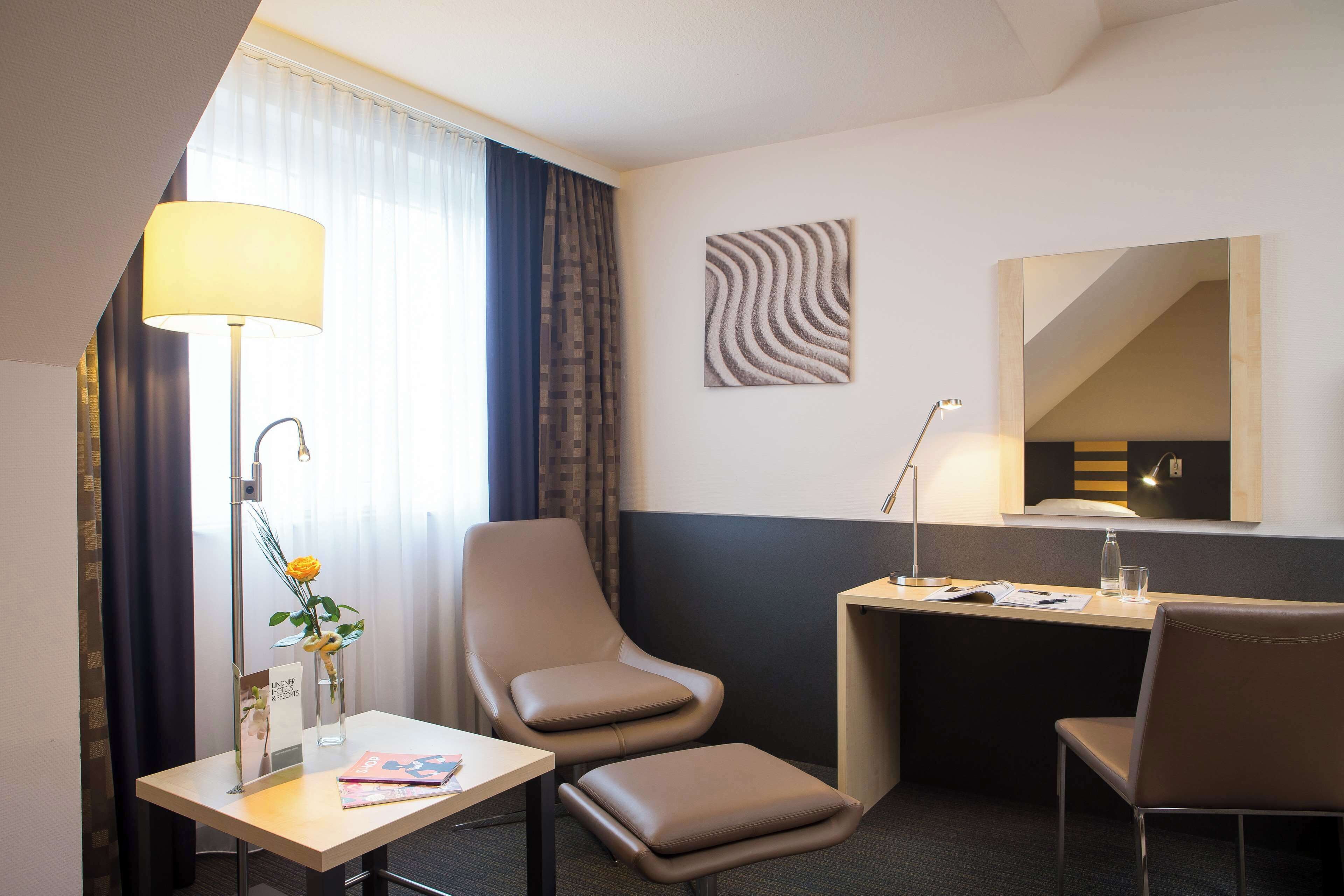 Hotelkamer met een bureau, twee stoelen, een lamp, een vaas met bloemen, een spiegel en een kunstwerk aan de muur.