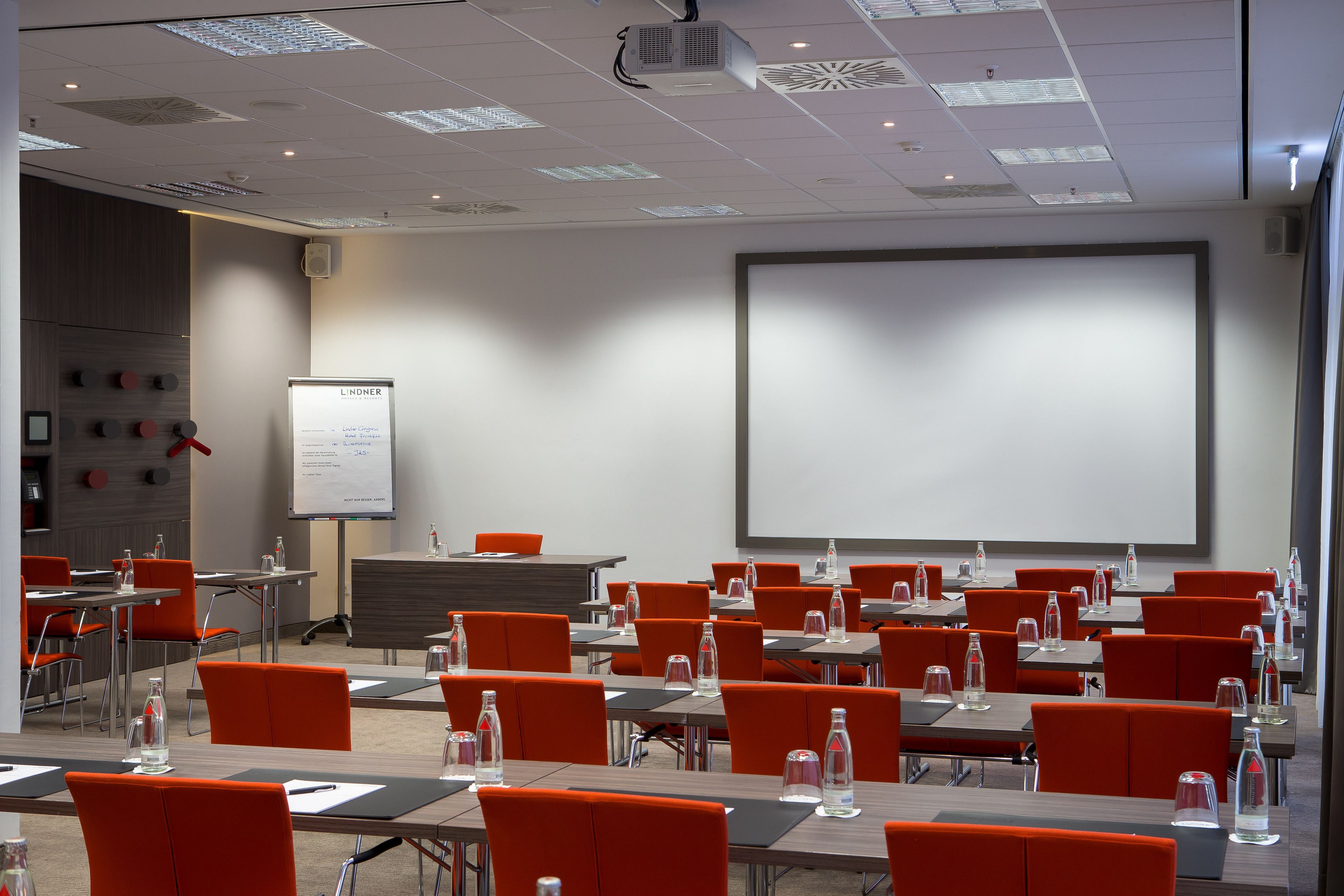 A conference room with rows of tables and chairs, a whiteboard, and a projector screen.