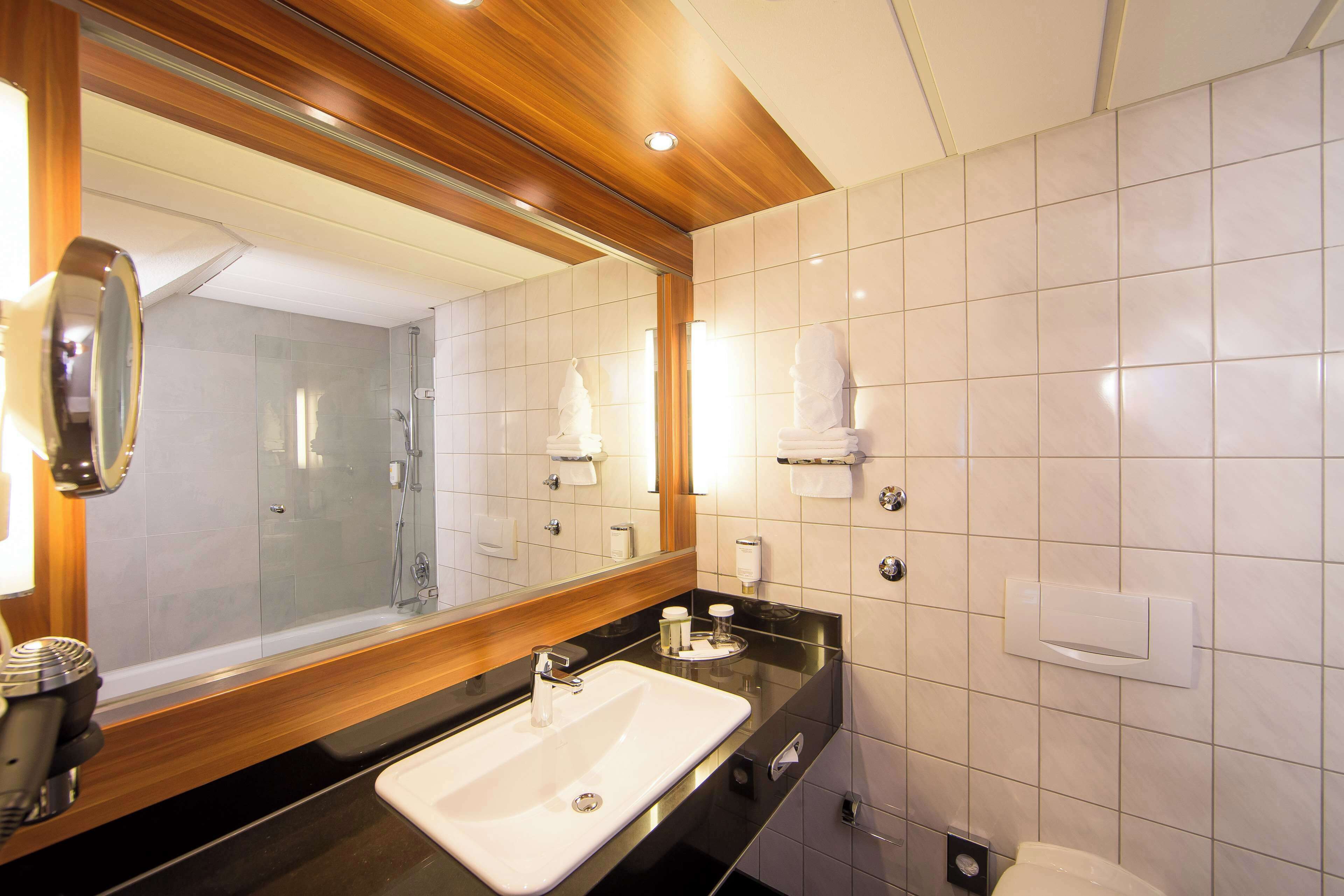 A modern bathroom with a large mirror, a sink, and a shower.