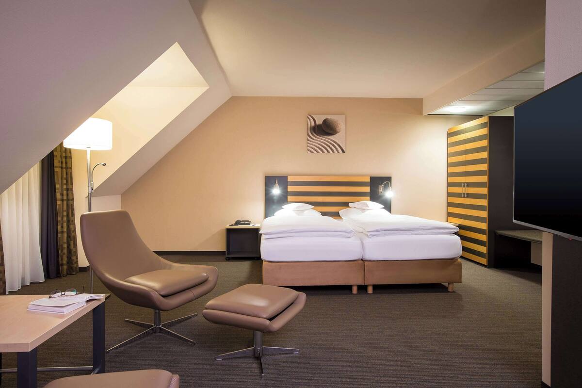 A hotel room with a bed, a desk, a chair, a TV, and a lamp.