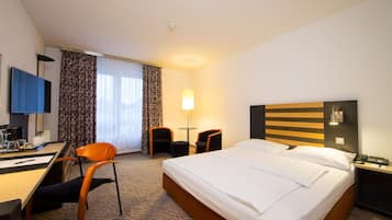 A hotel room with a bed, desk, chairs, a TV, and a lamp.