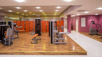 Ein Fitnessraum mit verschiedenen Trainingsgeräten, Holzboden und orangenen Raumteilen.