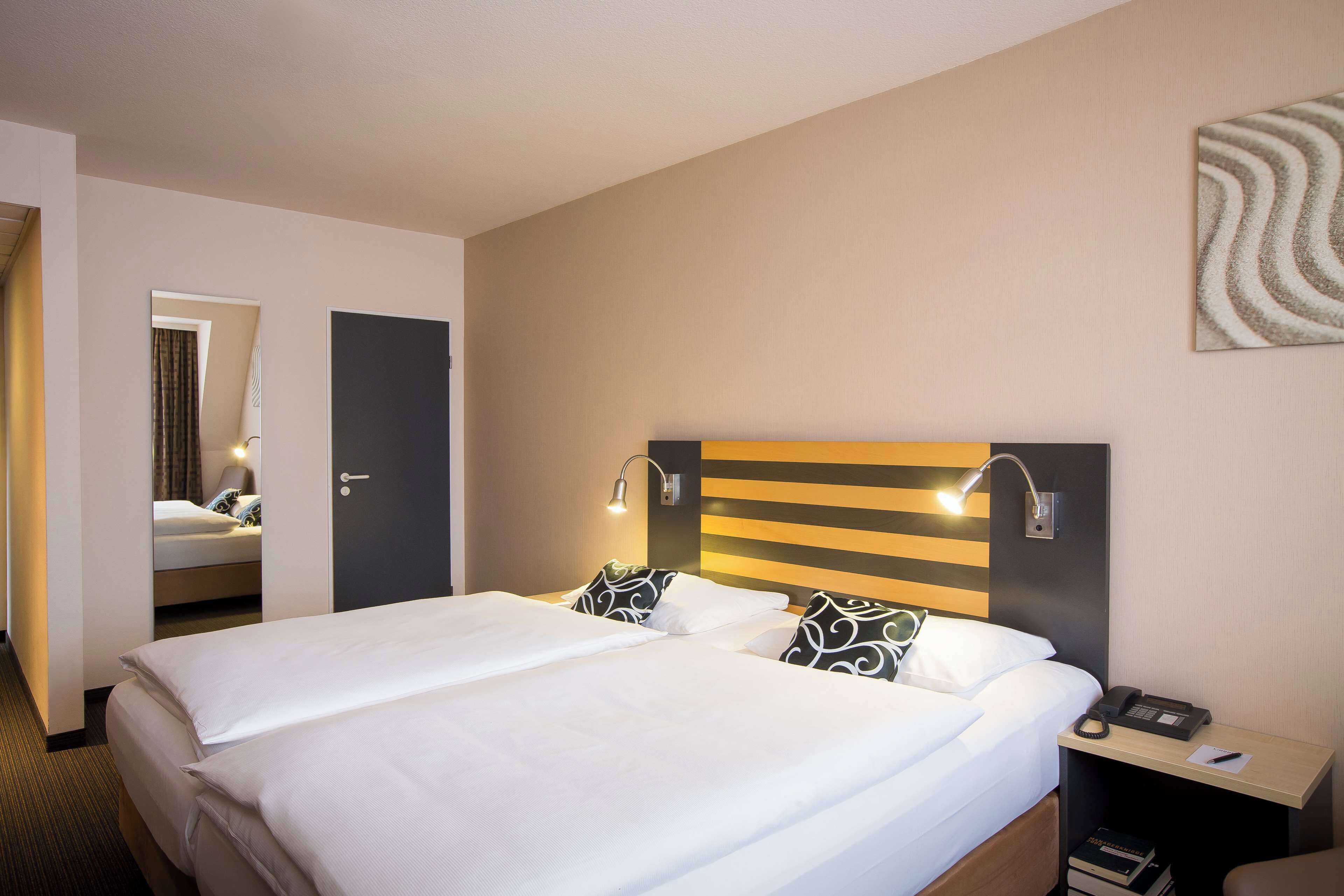 Ein Hotelzimmer mit einem großen Bett, Nachttischlampen, einem Telefon und einem Spiegel.