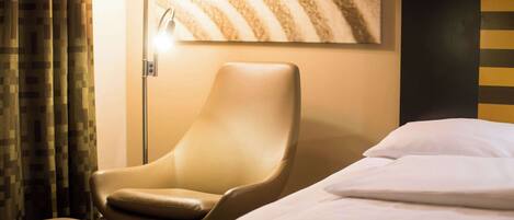 Habitación de hotel con una cama individual, un sillón de cuero, una lámpara de pie y una pared con diseño texturizado.