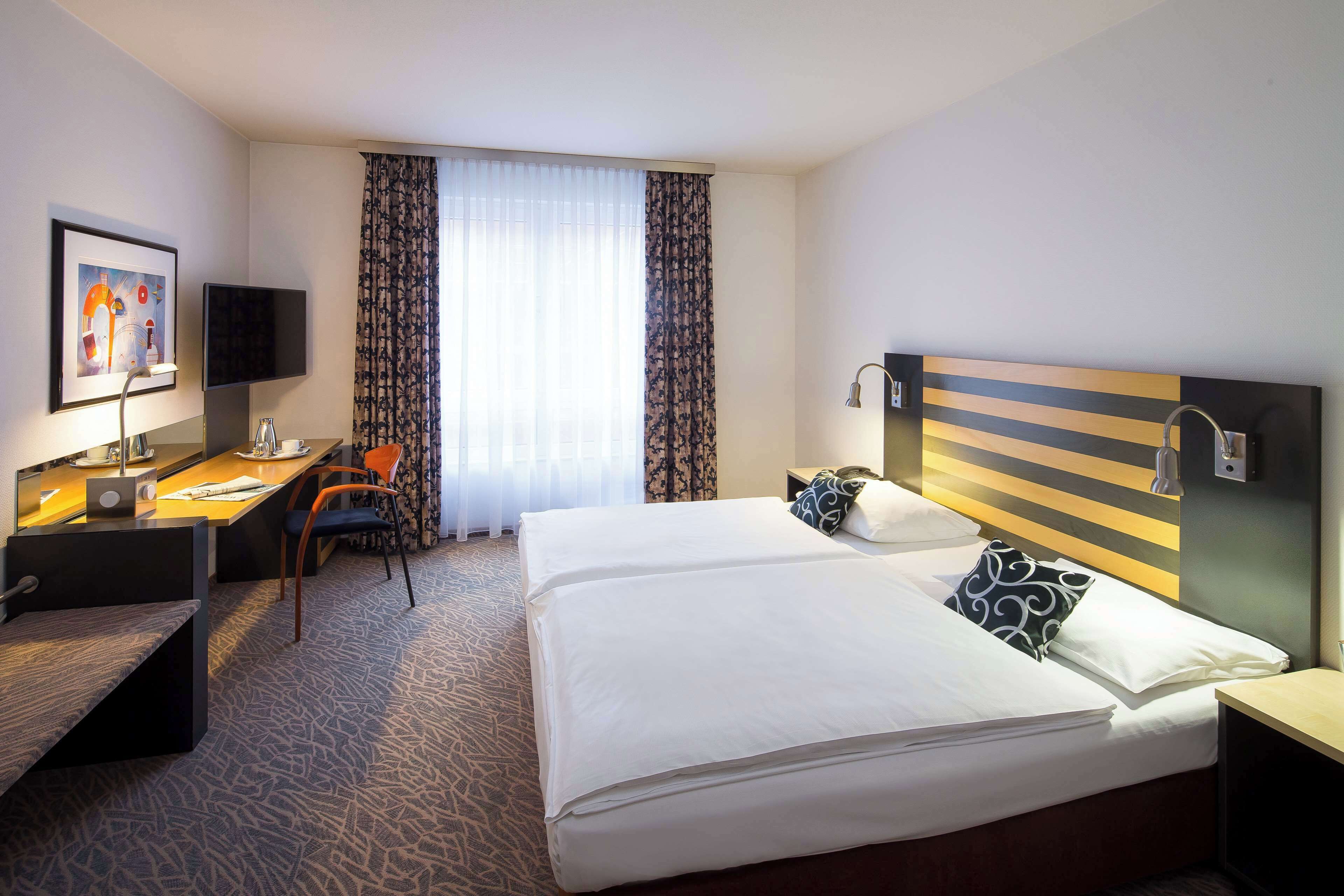 A hotel room with a bed, desk, chair, TV, and a window with curtains.