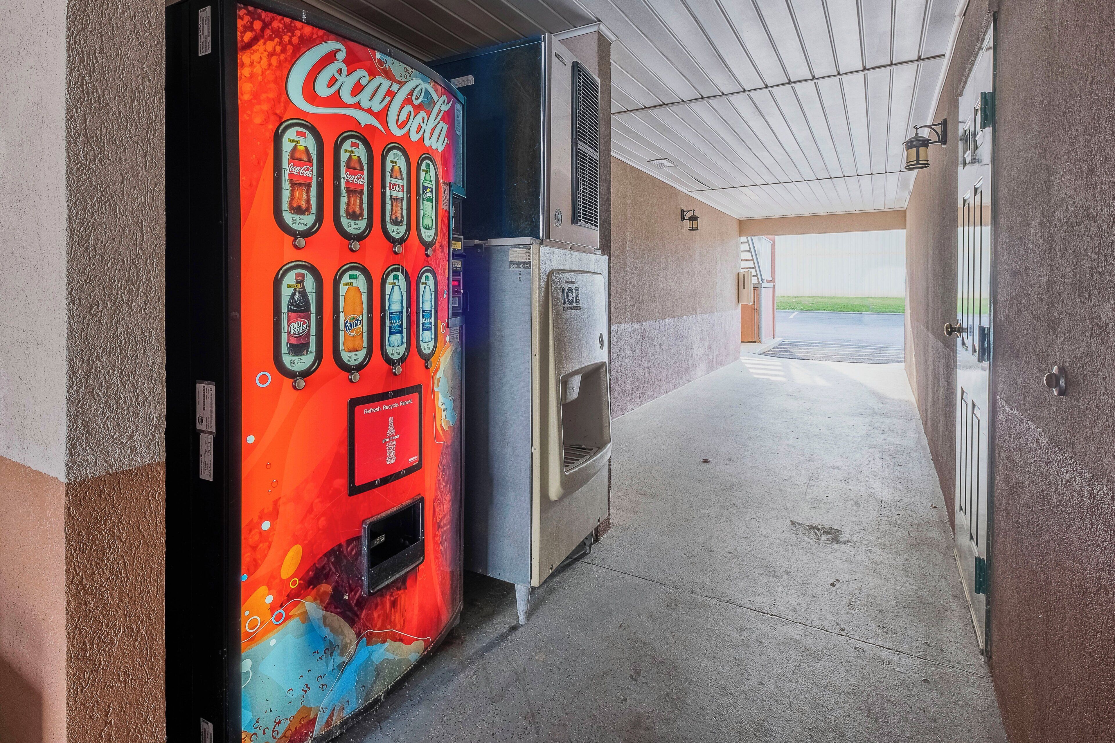 Máquina expendedora con el logotipo de Coca-Cola, un refrigerador y una puerta que da a un espacio exterior.