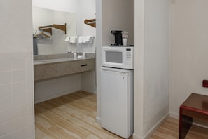 A compact kitchenette with a microwave and coffee maker, a small refrigerator, a countertop with a sink, and a wooden bench.
