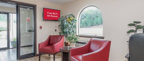 Un hall d’entrée avec deux fauteuils rouges, un panneau indiquant « Wi-Fi gratuit dans toutes les chambres », un panneau « Interdiction de fumer » et une grande fenêtre donnant sur la forêt.