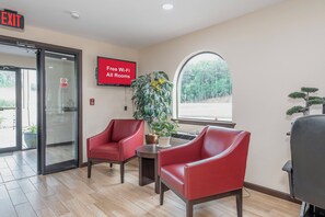 Um lobby com duas cadeiras vermelhas, um aviso de 'Wi-Fi Gratuito em Todos os Quartos', um aviso de 'Proibido Fumar' e uma grande janela com vista para árvores.