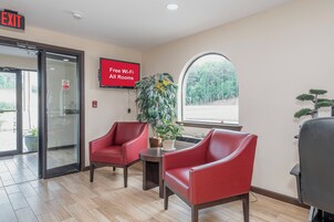 A lobby with two red chairs, a 'Free Wi-Fi All Rooms' sign, a 'No Smoking' sign, and a large window with a view of trees.