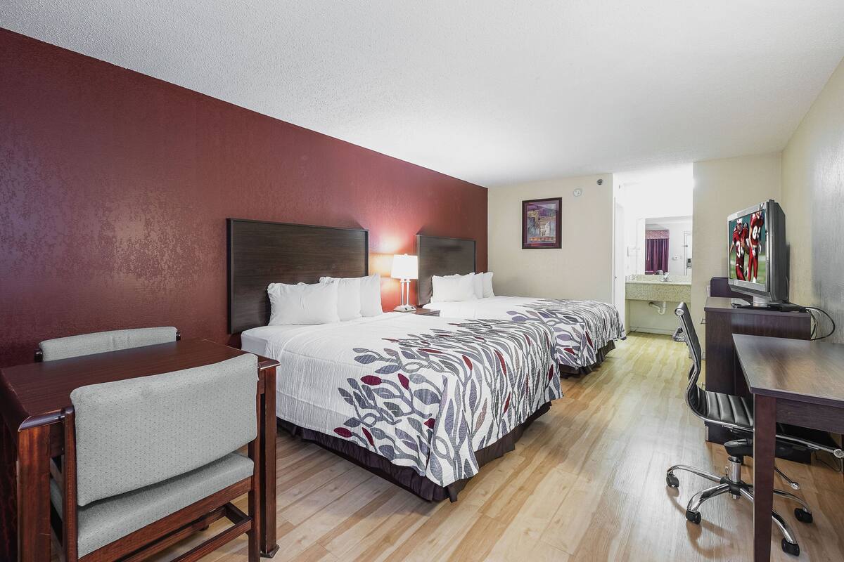 Quarto de hotel com cama, escrivaninha, cadeira e televisão.