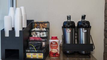 A coffee station with disposable cups, a coffee creamer dispenser, and two coffee machines.