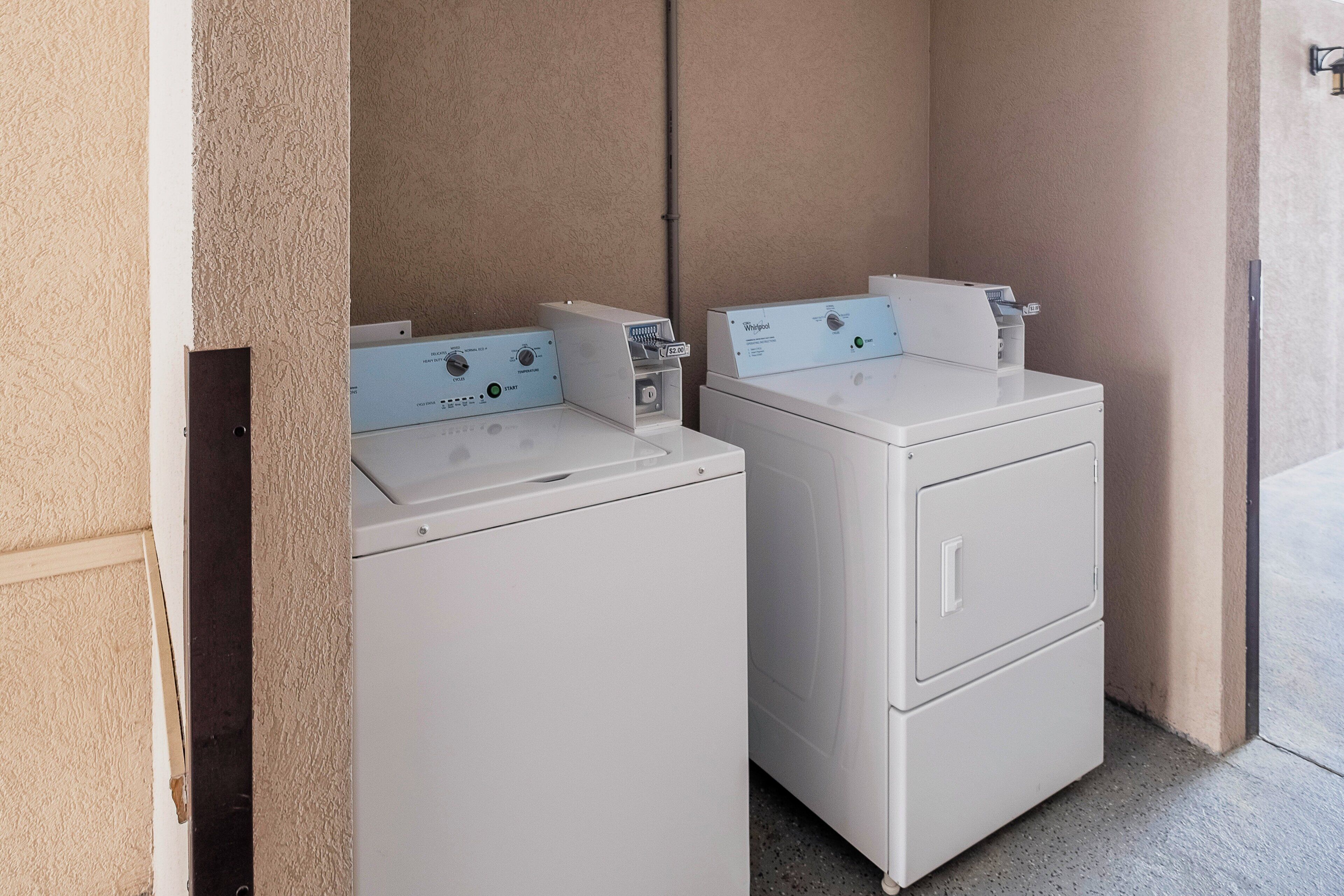 A laundry room with two stacked washers and dryers, a wall-mounted light fixture, and a door leading to another room.