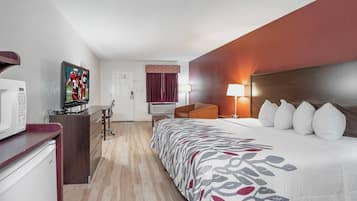 Quarto de hotel com cama, escrivaninha, televisão e micro-ondas.