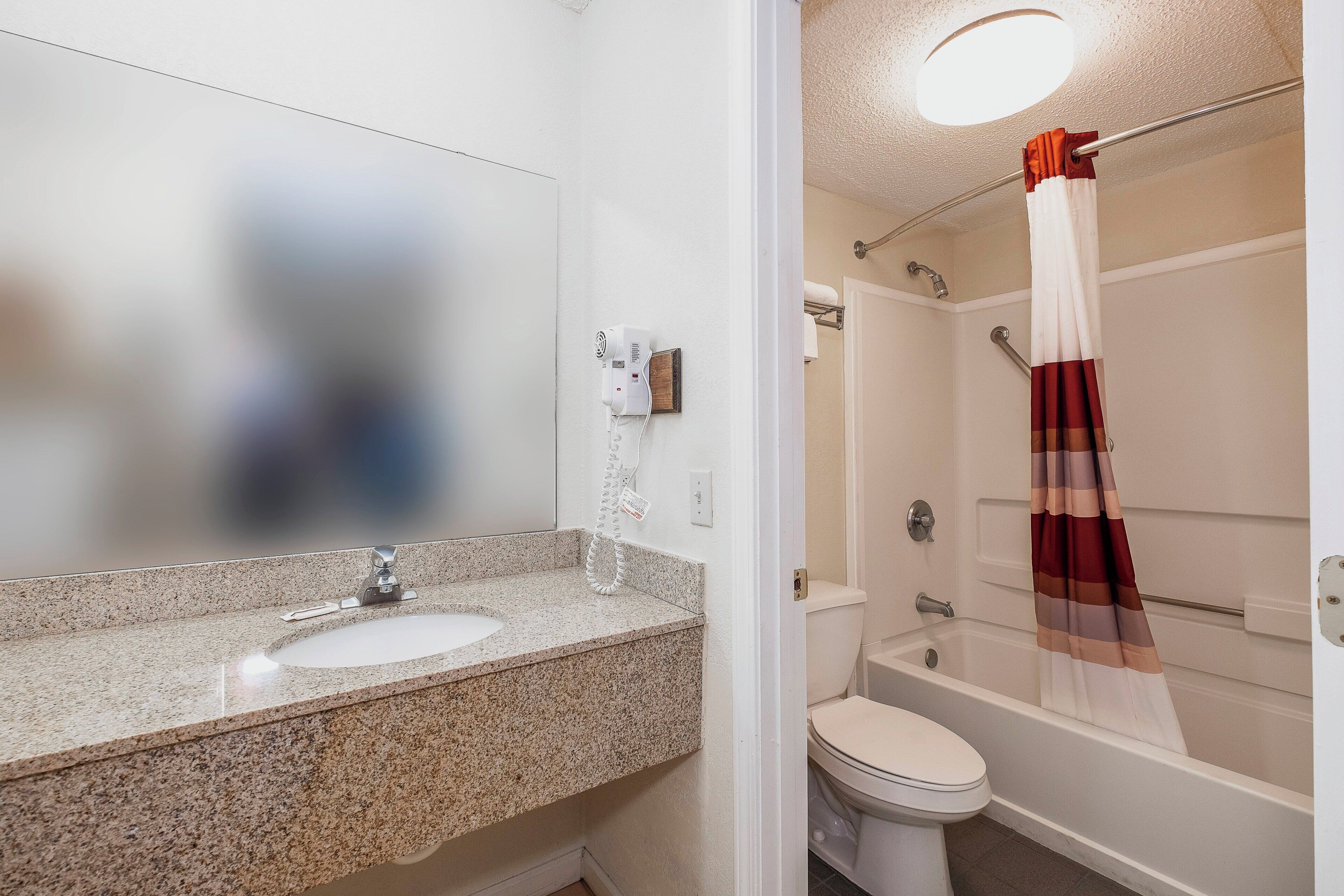 Un baño con lavamanos de encimera de granito, inodoro, ducha con puerta de cristal y toallero.